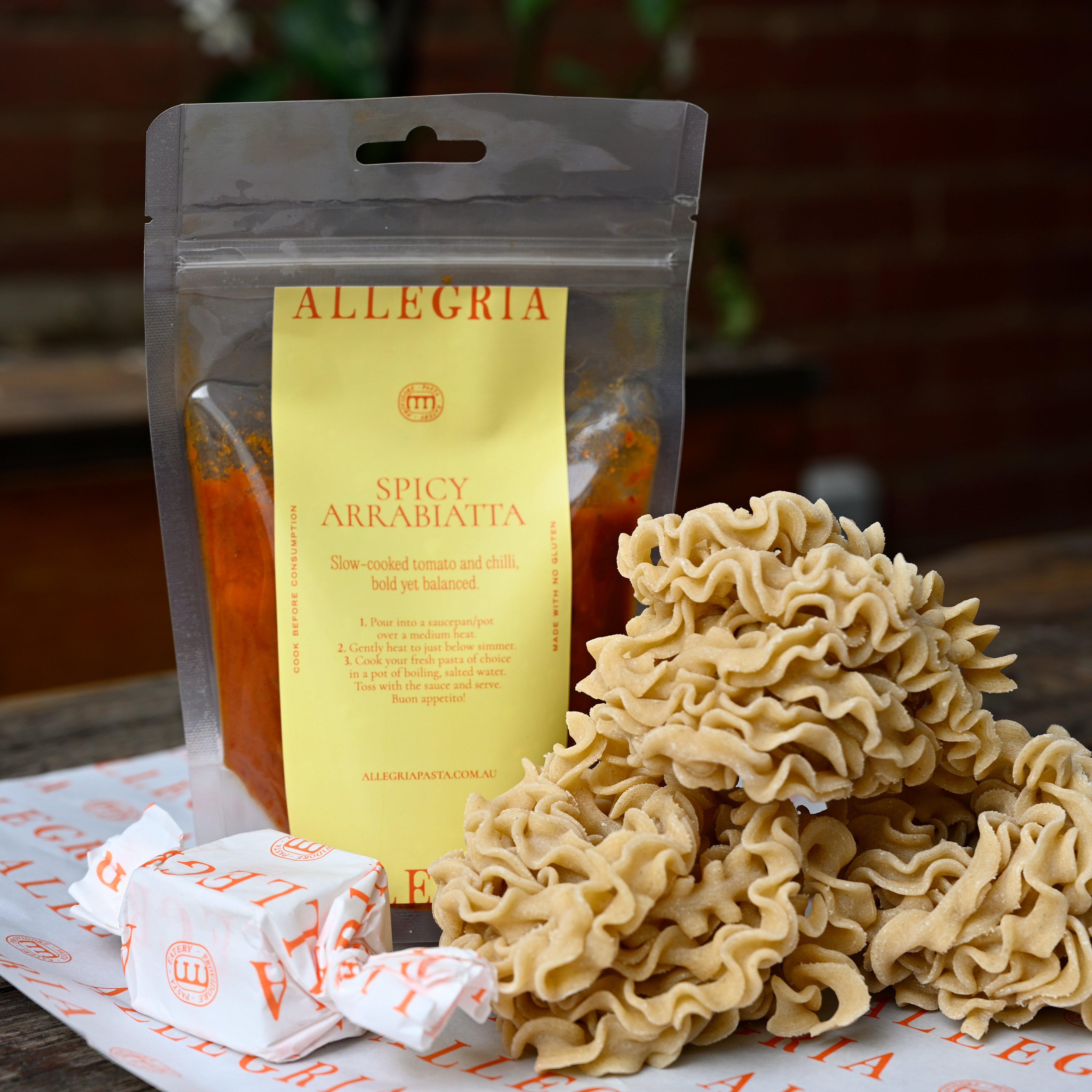 Spicy Arrabbiata and mafalde pasta with Allegria packaging on a wooden surface.